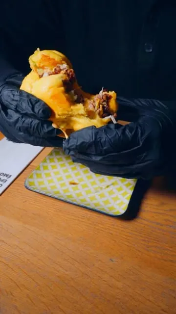 Burger ouvert tenu par des mains gantées