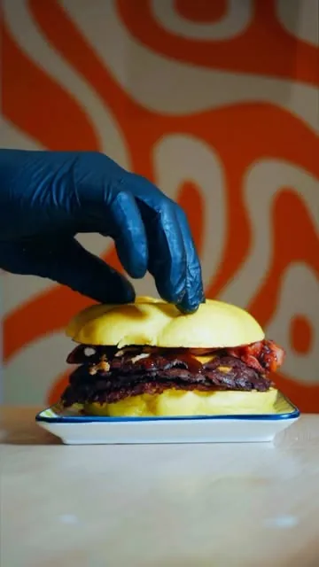Main gantée posée sur un burger devant le mur à vagues orange du restaurant